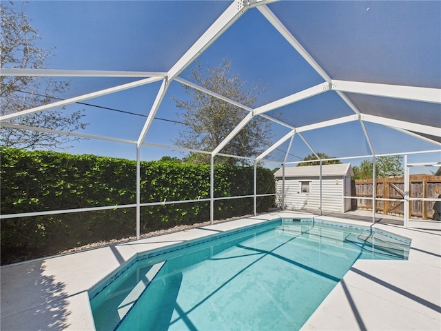 view of pool featuring a storage unit, an outbuilding, fence, glass enclosure, and a patio area