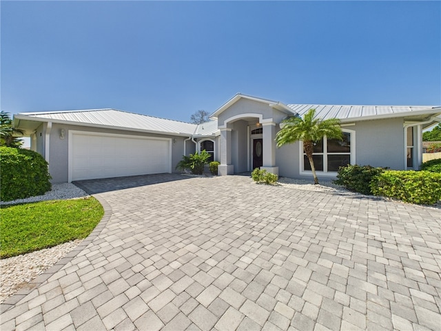 view of front facade featuring decorative driveway, metal roof, a garage, and stucco siding