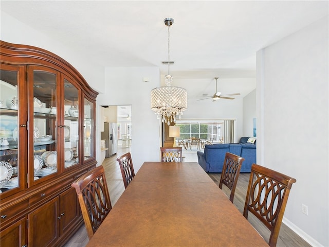 dining area with ceiling fan with notable chandelier, lofted ceiling, wood finished floors, and visible vents