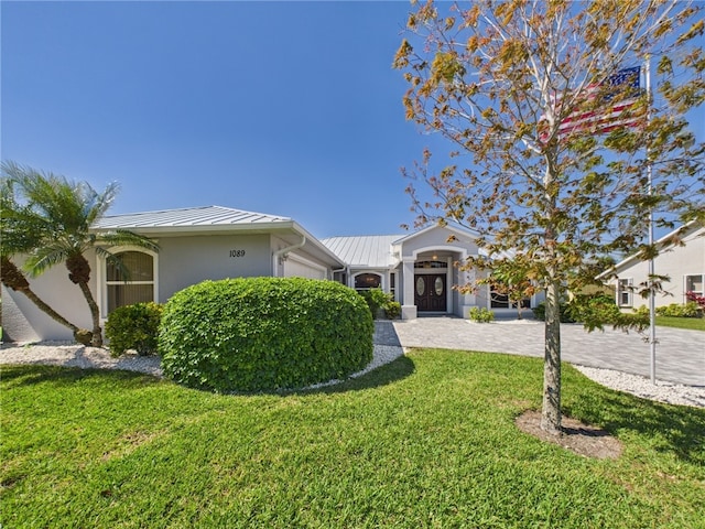 view of front of property with a front yard, stucco siding, metal roof, an attached garage, and a standing seam roof