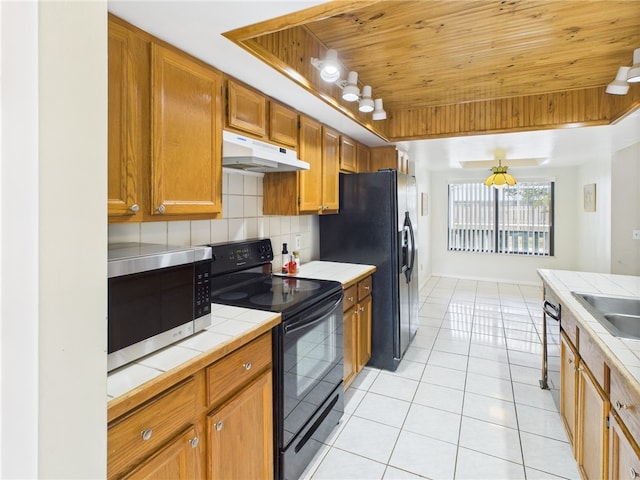 108 Cardinal Dr, Sebastian, FL 32958 - kitchen featuring black appliances, tile counters, under cabinet range hood, a raised ceiling, and light tile patterned flooring