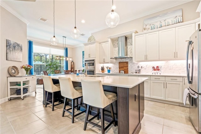 kitchen featuring tasteful backsplash, light countertops, ornamental molding, appliances with stainless steel finishes, and wall chimney exhaust hood