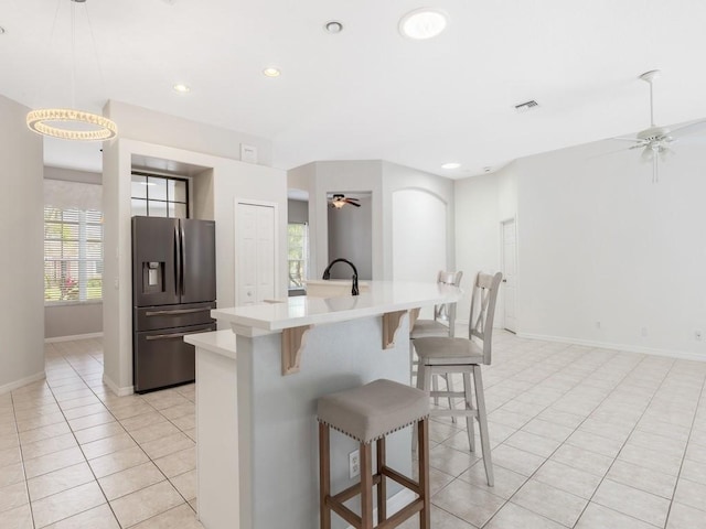 kitchen featuring a kitchen bar, stainless steel fridge with ice dispenser, ceiling fan, and a kitchen island with sink