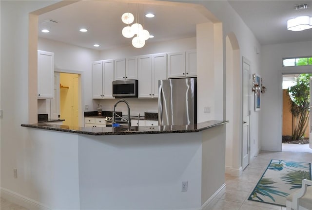 kitchen featuring dark stone countertops, hanging light fixtures, stainless steel appliances, white cabinets, and kitchen peninsula