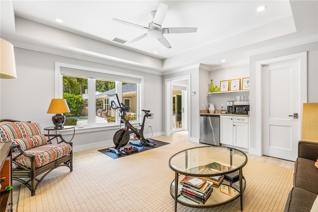 exercise room with a raised ceiling, crown molding, ceiling fan, and light wood-type flooring