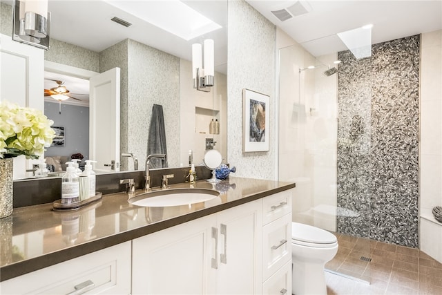 bathroom with ceiling fan, toilet, a tile shower, and vanity