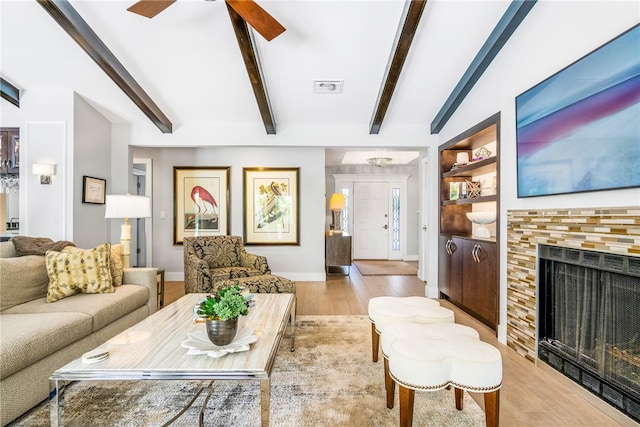 living room with a tile fireplace, vaulted ceiling with beams, light hardwood / wood-style flooring, and ceiling fan