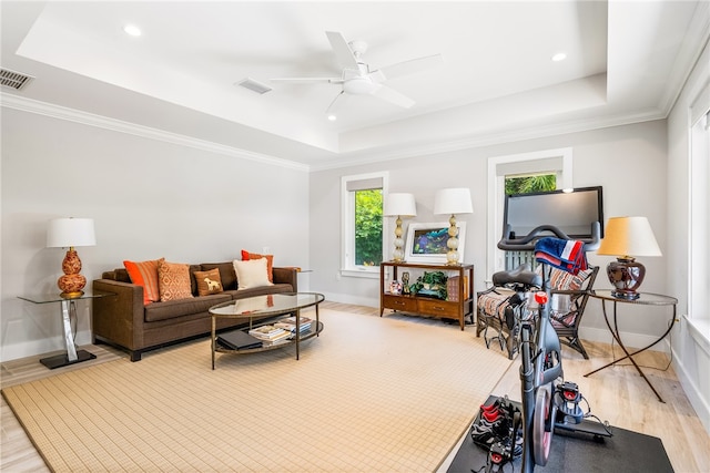 living room featuring a raised ceiling, crown molding, ceiling fan, and light wood-type flooring