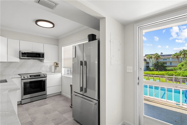 kitchen featuring stainless steel appliances, decorative backsplash, crown molding, light stone countertops, and white cabinetry