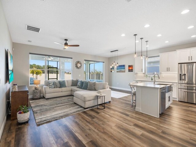 living room featuring visible vents, a healthy amount of sunlight, a ceiling fan, and dark wood finished floors