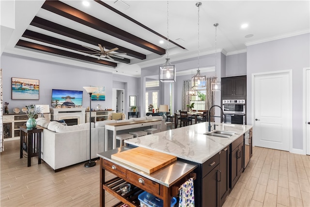 kitchen featuring sink, an island with sink, beamed ceiling, double oven, and light stone countertops