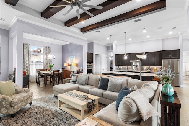 living room with ornamental molding, light wood-type flooring, beamed ceiling, and ceiling fan