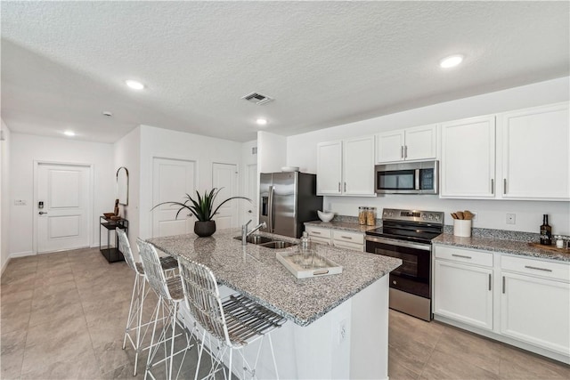 kitchen featuring a breakfast bar area, a kitchen island with sink, stainless steel appliances, and a textured ceiling