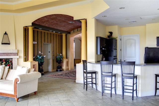 kitchen featuring decorative columns, crown molding, a breakfast bar, and black appliances