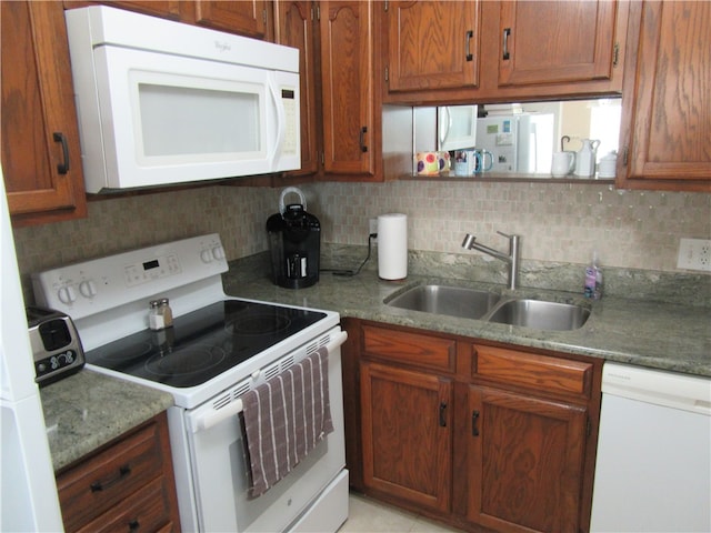 kitchen with decorative backsplash, light stone counters, sink, and white appliances