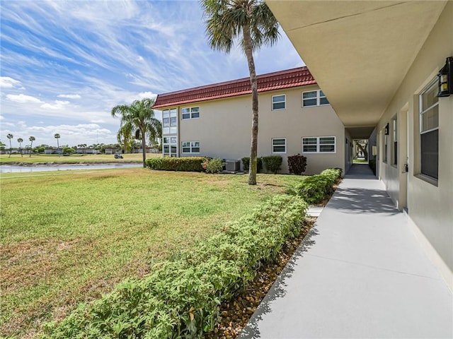 view of side of property with a water view, cooling unit, stucco siding, a tile roof, and a yard