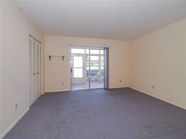 carpeted empty room featuring a textured ceiling and baseboards