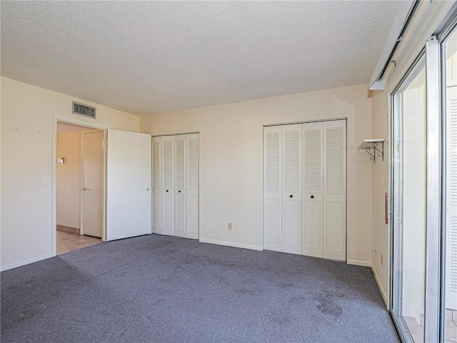 unfurnished bedroom featuring light carpet, a textured ceiling, and multiple closets