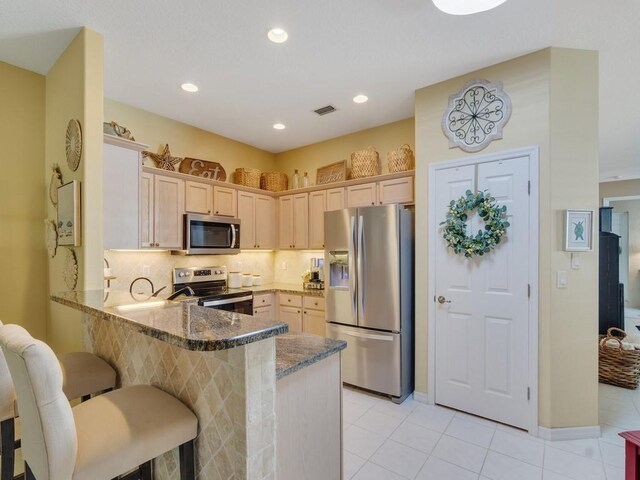 7639 15th Ln, Vero Beach, FL 32966 - kitchen featuring stainless steel appliances, a peninsula, dark stone counters, light tile patterned floors, and a breakfast bar area