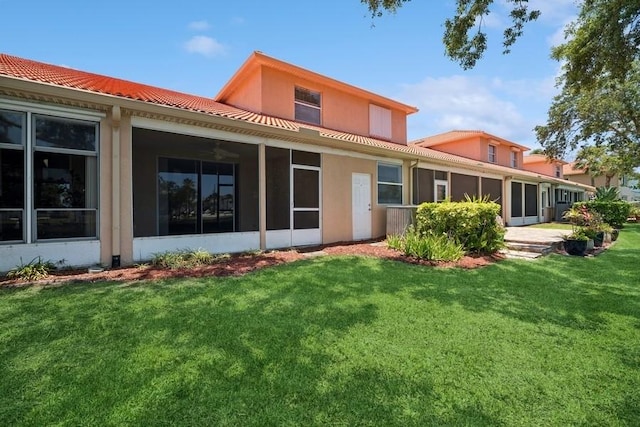 back of property featuring a sunroom, a lawn, stucco siding, and a tiled roof