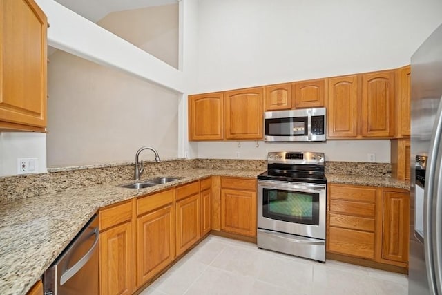 kitchen featuring appliances with stainless steel finishes, light stone countertops, light tile patterned floors, high vaulted ceiling, and brown cabinetry