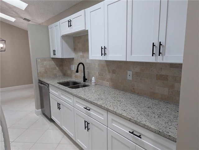 kitchen with a sink, a skylight, stainless steel dishwasher, light tile patterned floors, and white cabinets