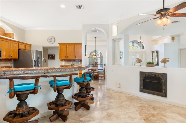 kitchen with stainless steel fridge with ice dispenser, decorative backsplash, a fireplace, and ornamental molding