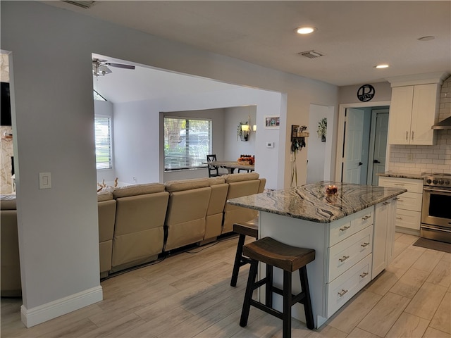 kitchen with light hardwood / wood-style floors, a center island, white cabinets, light stone countertops, and stainless steel electric range oven