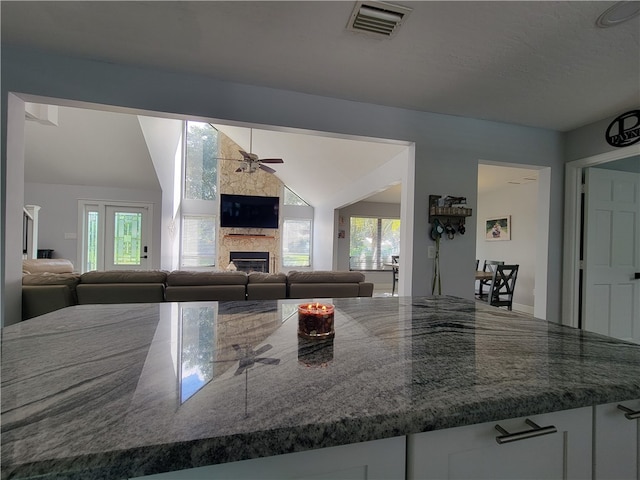 kitchen with a fireplace, ceiling fan, white cabinetry, and lofted ceiling