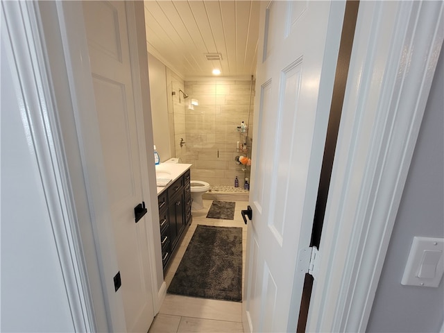 bathroom with toilet, vanity, tile patterned floors, and a tile shower