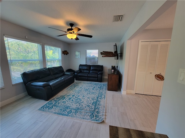 living room featuring a textured ceiling, light wood-type flooring, and ceiling fan