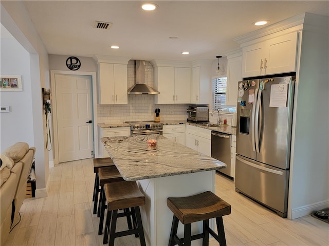 kitchen with stainless steel appliances, a center island, white cabinets, wall chimney exhaust hood, and hanging light fixtures