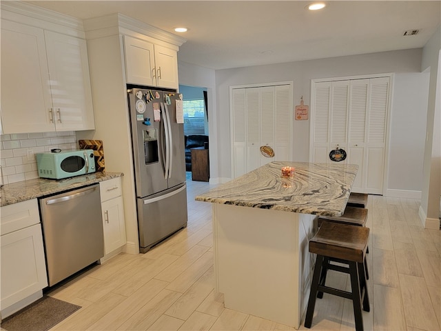 kitchen featuring light stone counters, stainless steel appliances, white cabinetry, light hardwood / wood-style floors, and a center island