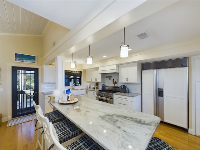 kitchen featuring white cabinetry, a kitchen bar, premium appliances, hanging light fixtures, and light stone countertops