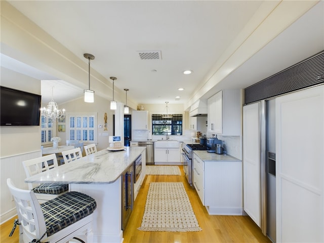 kitchen with built in appliances, light stone countertops, white cabinets, a kitchen island, and decorative light fixtures