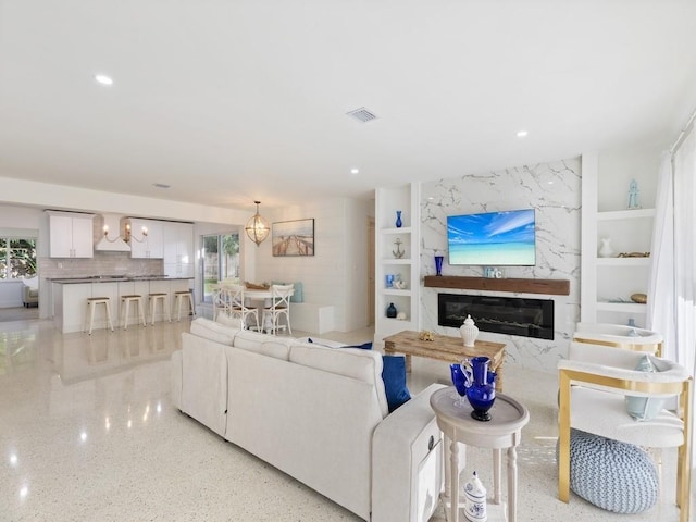 living area with a fireplace, visible vents, light speckled floor, and a wealth of natural light