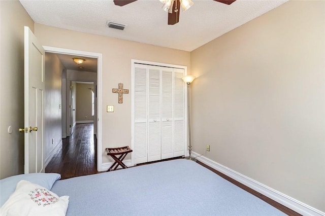 bedroom with dark hardwood / wood-style flooring, ceiling fan, a closet, and a textured ceiling