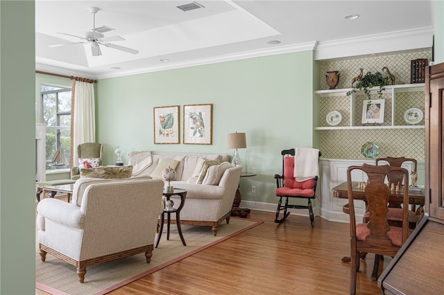 living area with ornamental molding, visible vents, ceiling fan, and wood finished floors