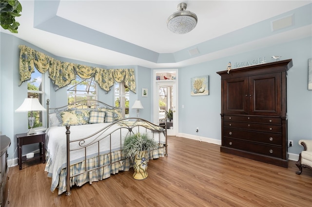 bedroom with wood finished floors, a raised ceiling, visible vents, and baseboards