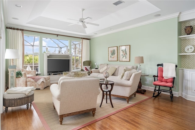 living area featuring a tray ceiling, crown molding, visible vents, a ceiling fan, and wood finished floors