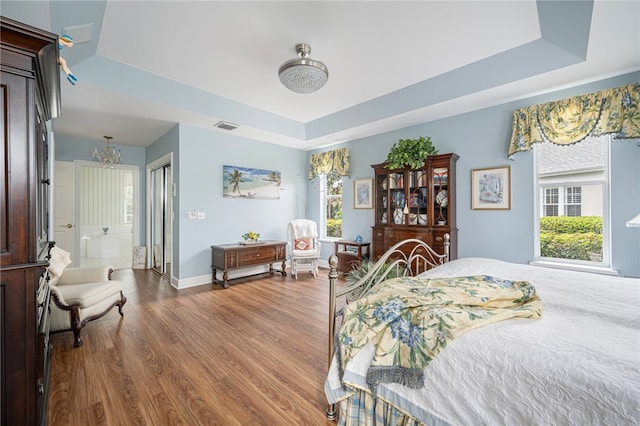 bedroom featuring wood finished floors, a raised ceiling, visible vents, and baseboards