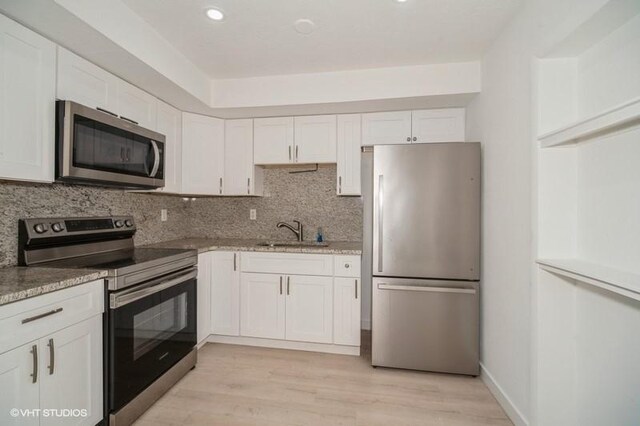 7645 58th Ave, Vero Beach, FL 32967 - kitchen featuring light wood finished floors, a sink, backsplash, white cabinetry, and appliances with stainless steel finishes