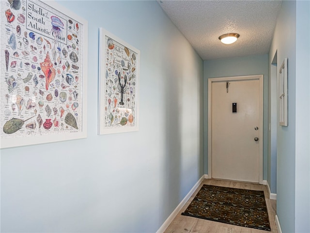 doorway featuring a textured ceiling, baseboards, and wood finished floors