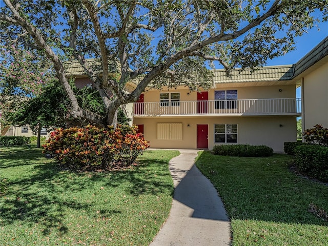 multi unit property with a balcony, a front lawn, and stucco siding