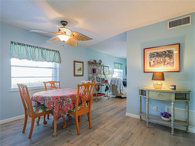 dining space featuring a textured ceiling, wood finished floors, a ceiling fan, visible vents, and baseboards