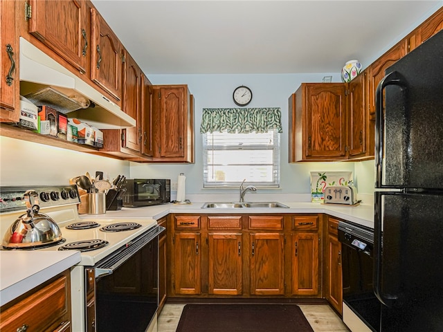 kitchen featuring brown cabinetry, under cabinet range hood, light countertops, black appliances, and a sink