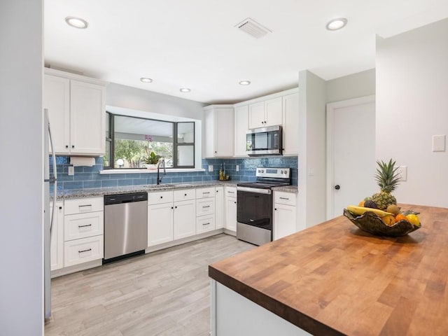 kitchen featuring appliances with stainless steel finishes, visible vents, wood counters, and decorative backsplash