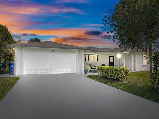 ranch-style home featuring a garage, driveway, a yard, and stucco siding