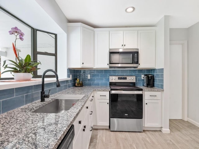 kitchen with a sink, white cabinets, appliances with stainless steel finishes, decorative backsplash, and light stone countertops