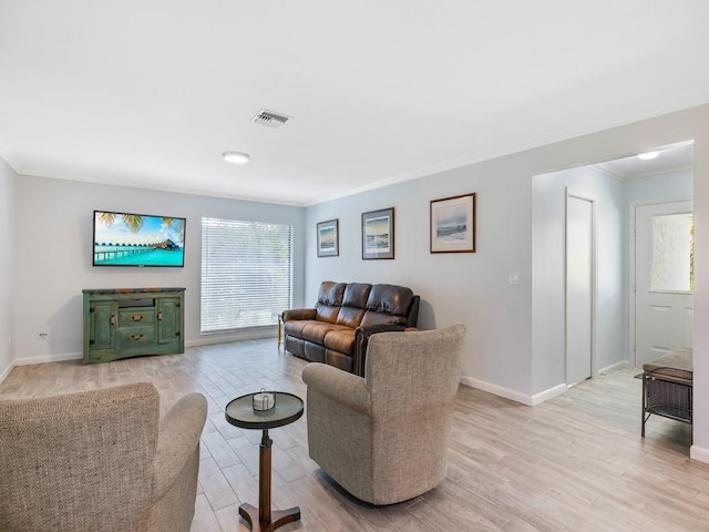 living area with ornamental molding, light wood-style flooring, plenty of natural light, and visible vents